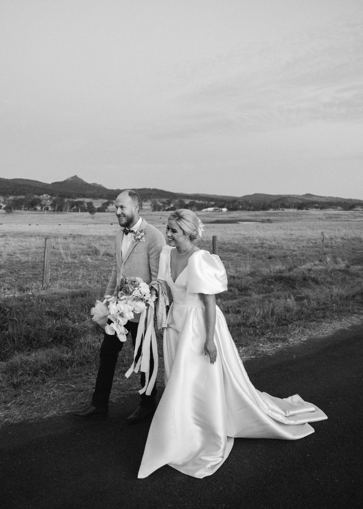 KWH real bride Izzy and Jake walking down a road together. She wears a modern aline wedding dress, Taryn Camille.
