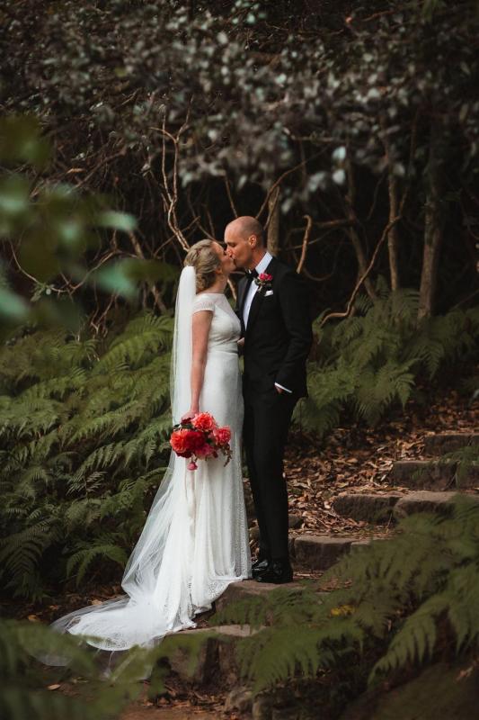 KWH real bride Gemma and Rob kiss in the woods. She wears the Jemma gown, a illusion neckline lace wedding dress.