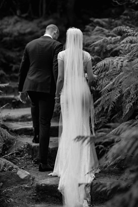 B&W image of KWH Real bride Gemma and Rob walking up outdoor stairs. She wears the Jemma gown, a modern fit and flare lace wedding dress.