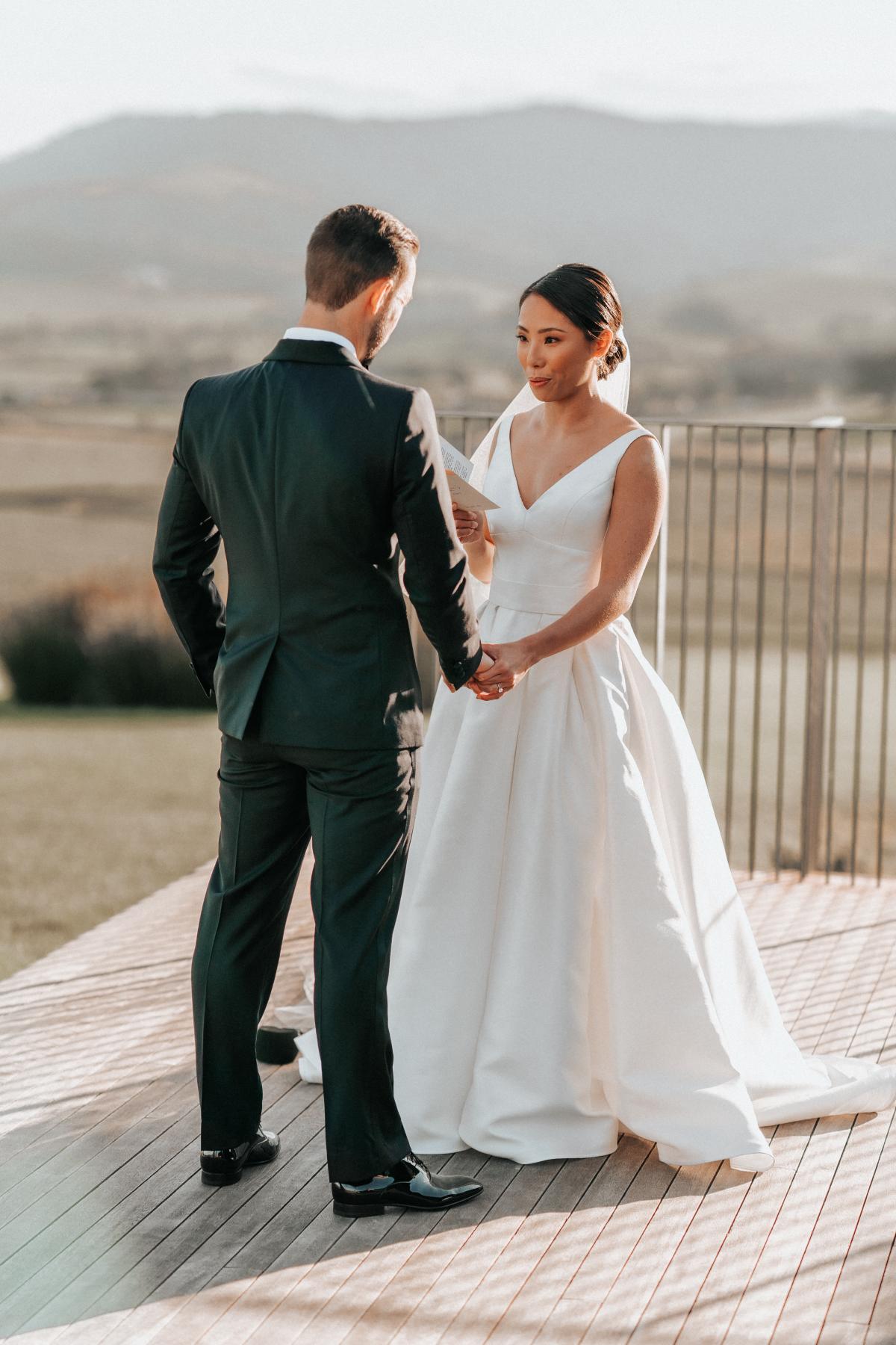 KWH real bride Rebecca takes as breath as she reads her vows to her husband. She wears the classic Leonie Melanie gown, a V-neck modern a-line wedding dress.
