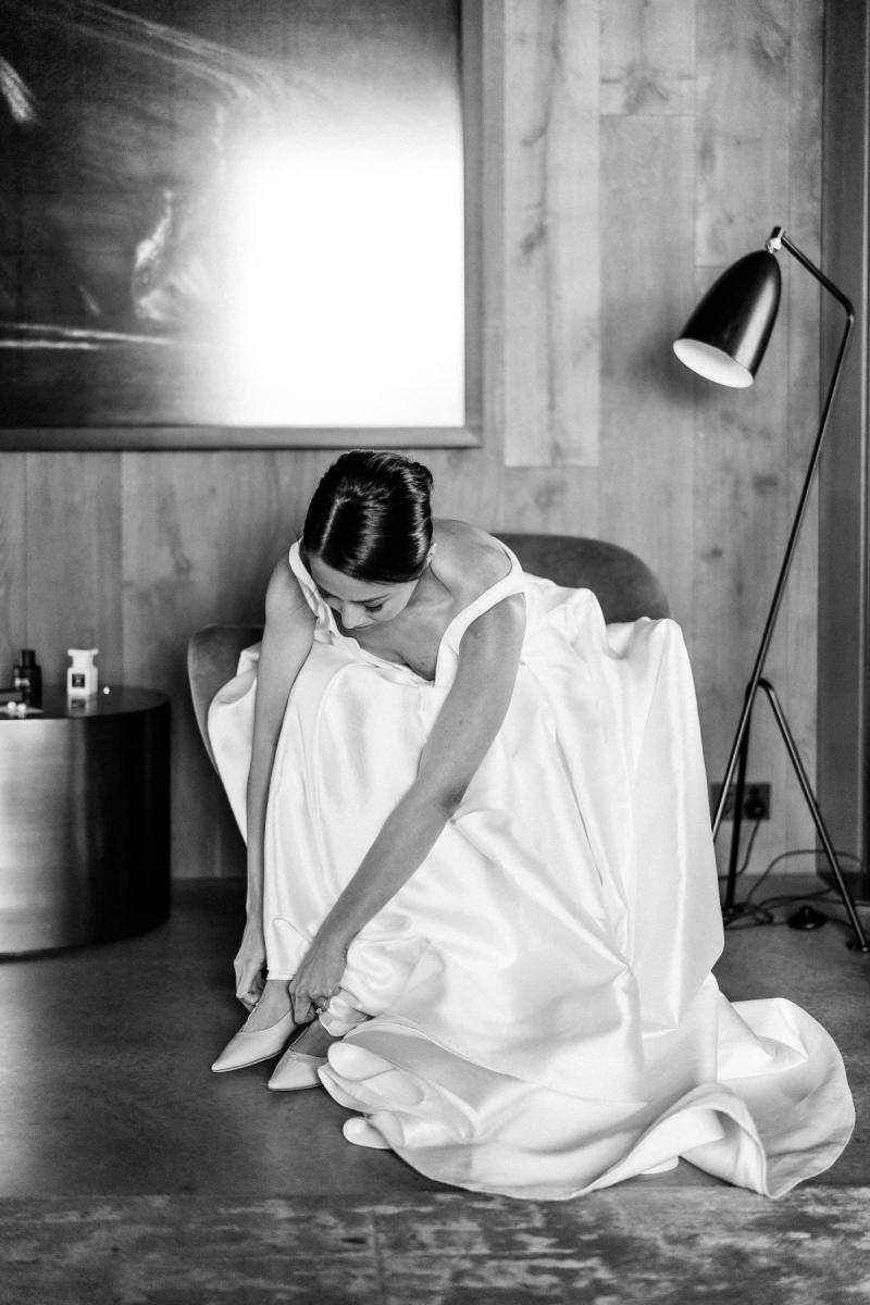 B&W image of KWH real bride Rebecca putting on her bridal shoes in her classic Leonie Melanie gown, a modern bridal ballgown with long train.