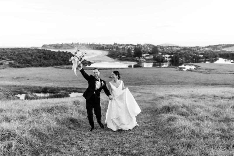 B&W image of KWH real bride Rebecca and Matthew throwing their flowers in the air in celebration. She wears the Leonie Melanie gown, a classic v-neck ball gown wedding dress.