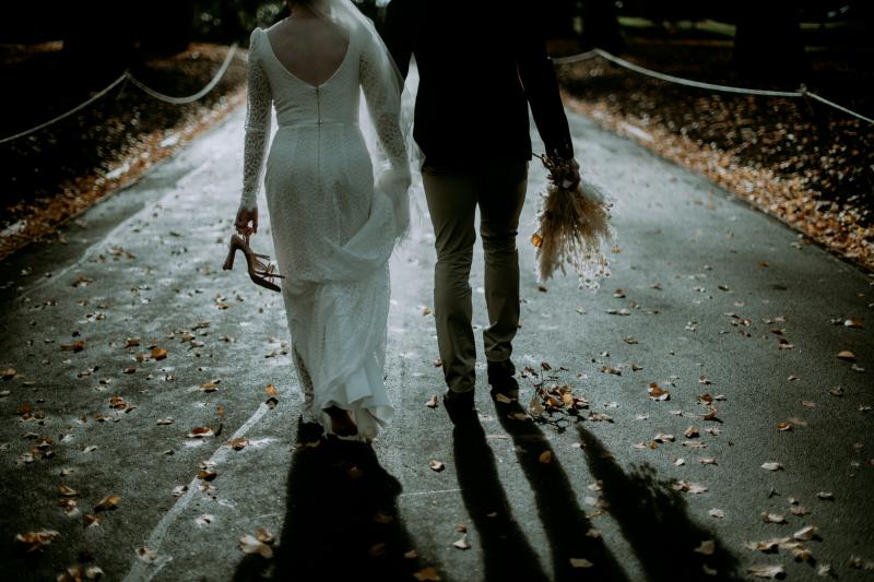 KWH real bride Rachel walks with josh down a wooded path. She wears the classic Rylie gown, a modern lace long sleeve wedding dress