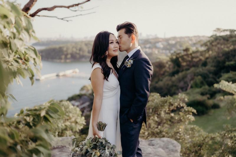KWH real bride Vicki and Tom holding one another on a cliff edge. She wears the Arabella gown, lunging neckline simple wedding dress.