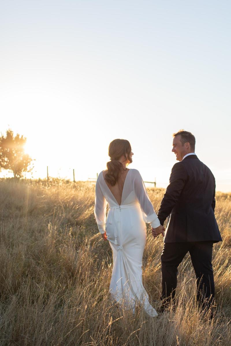 KWH real bride Erin and Stephen walk into the sunset. She wears the modern Brie gown, simple wedding dress with high neck and long sleeves..