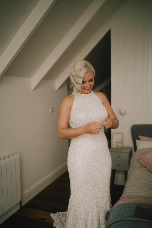 KWH real bride Laura putting on her jewellery after dressing in her Cindy gown, The Cindy gown, halter neck beaded wedding dress
