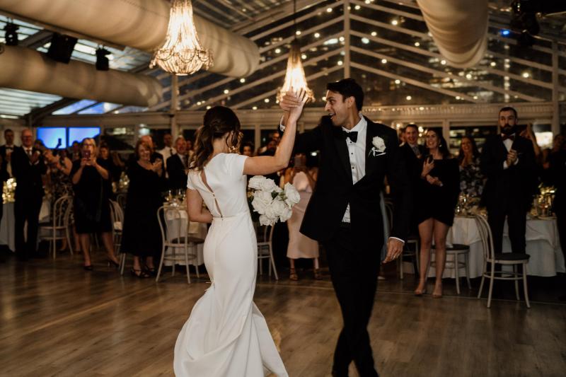 KWH real bride Jacqui and Chris dance at their reception. She wears the Clarissa gown, a high back fit and flare cap sleeve wedding dress.