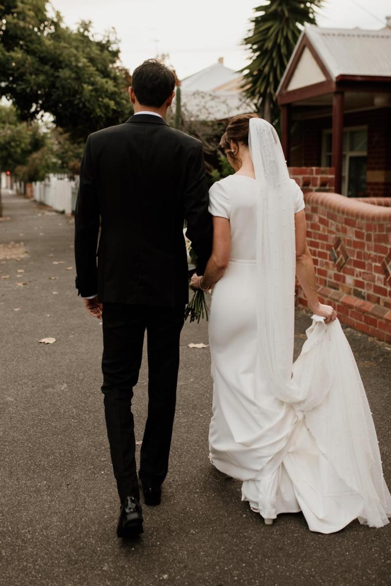 KWH real bride Jacqui and Chris walk down the street as she wears her ivory Clarissa gown, a fit and flare cap sleeve wedding dress.