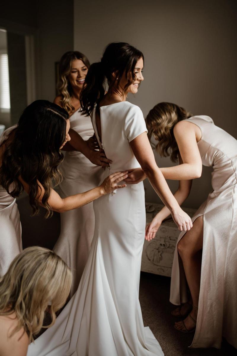 KWH real bride Jacqui has her bridesmaids help her put on her Clarissa gown, a minimalist fit and flare wedding dress.