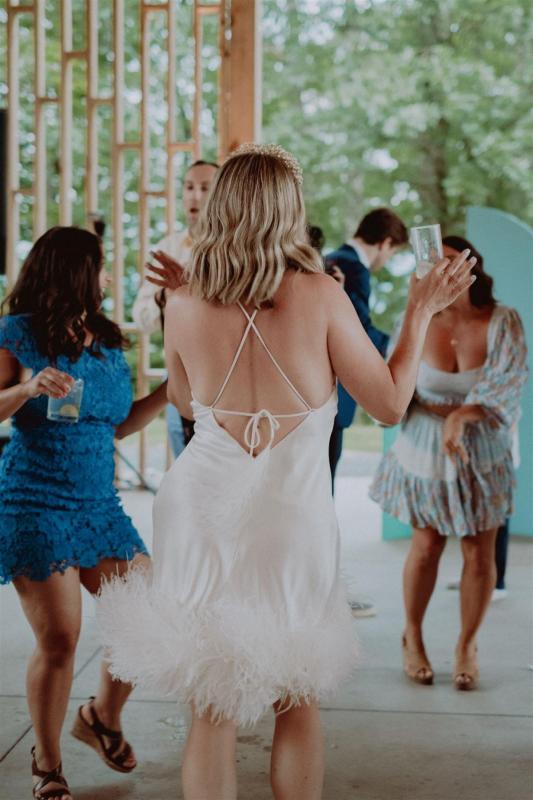 KWH real bride Kasey dances at her reception in her Sherry gown, a simple short wedding dress with open back and feather detail