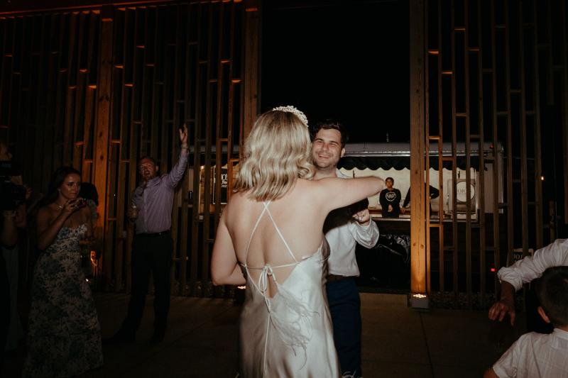 KWH real bride Kasey and Brian dancing at their reception as she wears the Sherry mini gown, a simple short wedding dress with open back and feather detail.