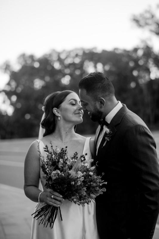 B&W image of KWH real bride Tara and Chris about to kiss. She wears the grand Taryn Camille gown; a modern aline wedding dress with satin buttons.