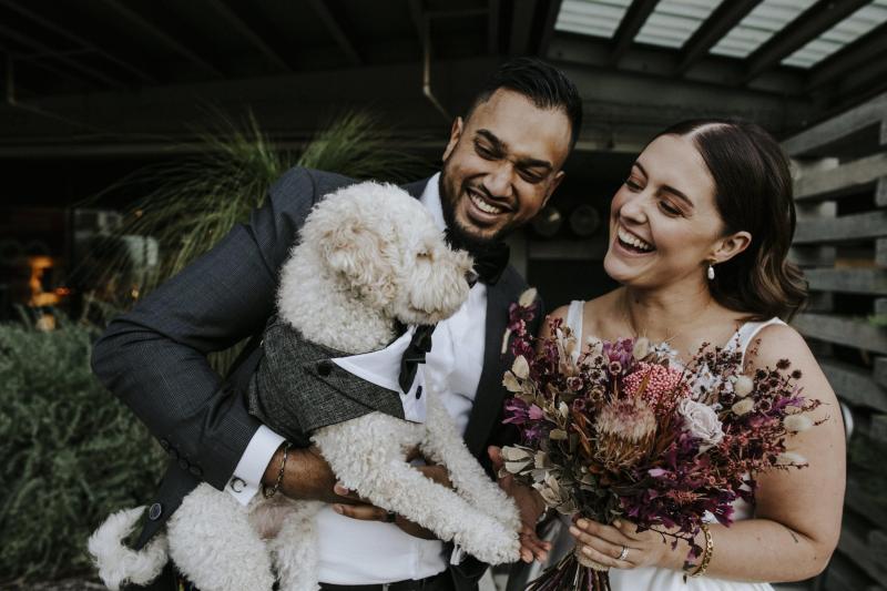 KWH real bride Tara and Chris hug their dog. She wears the Taryn Camille gown, a modern aline wedding dress with a U-shaped neckline