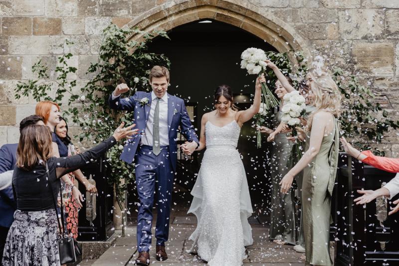 KWh real bride Monica and James leave the castle to thrown petals. She wears the ivory Anya gown, a classic sequin wedding dress with fitted silhouette.