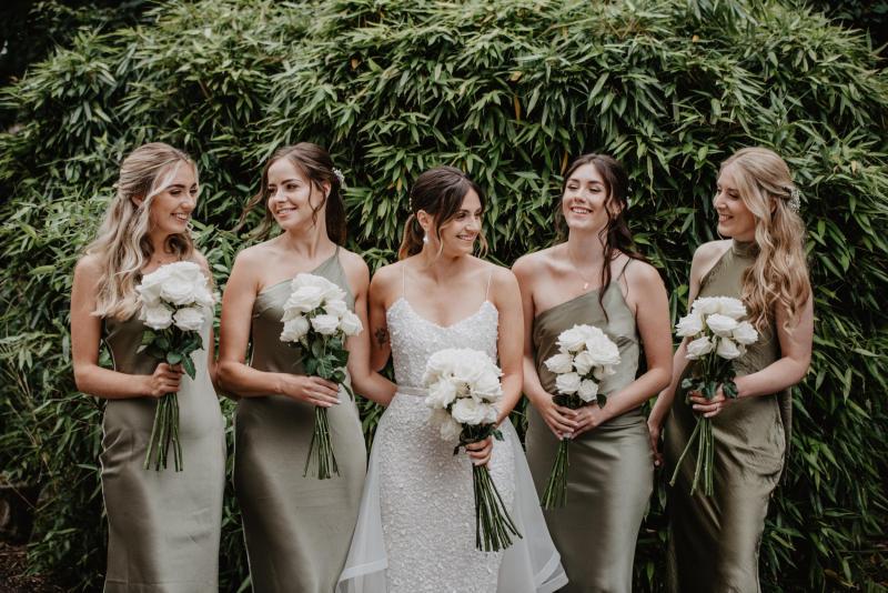 KWH real bride Monica stands with her bridesmaids who wear green silk bridesmaids dresses. She wears the Anya gown, a V-neck fit and flare sequin wedding dress.