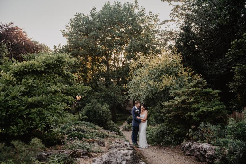 KWH real bride Monica and James ksis in the garden. She wears the Anya gown, an ivory elegant fit and flare wedding dress.