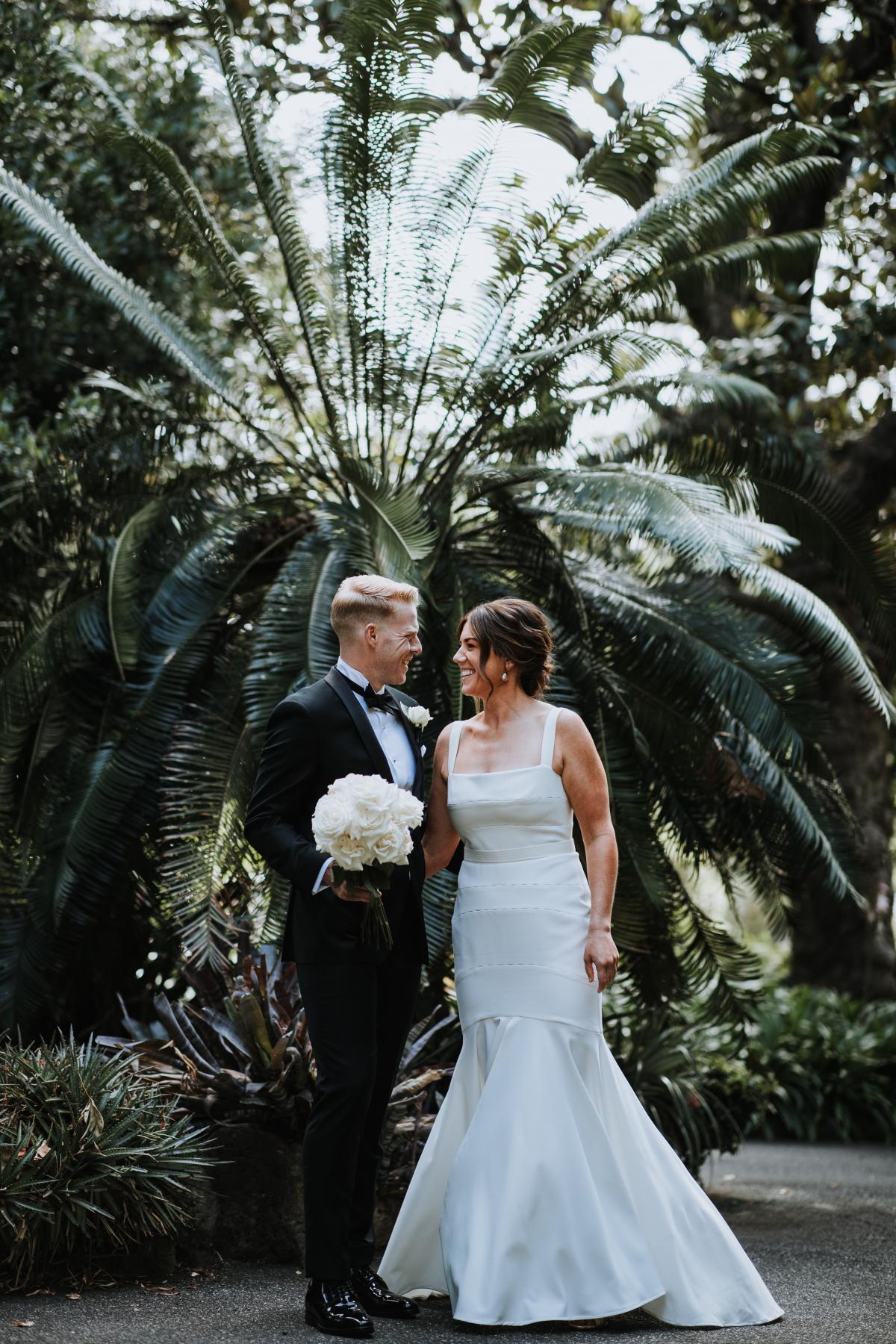 Real bride Emily and Dan share a moment in from of the palms. She wears the Violet dress by KWH, a square neckline dress with center split.