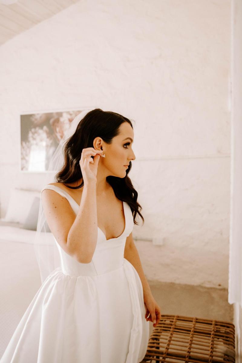 KWH real bride Shenea puts on her earring from Ruby & Sage to finish off her look. She wears the trendy Taryn Camille gown.