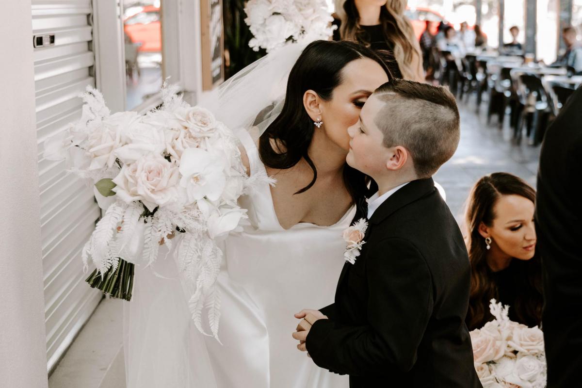 Real bride Shenea kissing her son on the cheek. She wears the modern Taryn Camille gown by KWH with a-line silhouette.