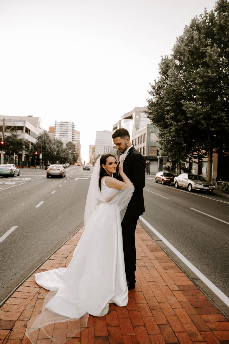 KWH real bride Shenea and Lain hug while standing on a median in the street. She wears the modern Taryn Camille gown by KWH with a-line shape and scoop back..