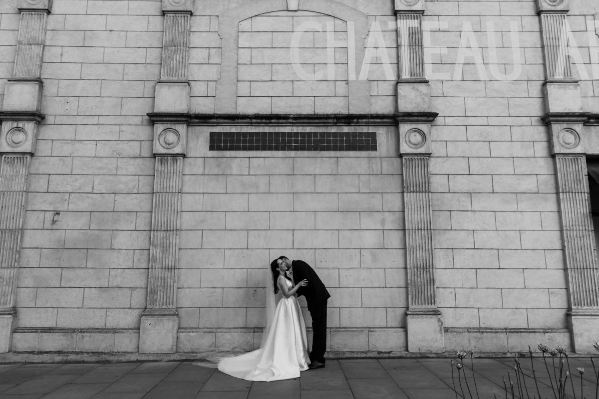 Real bride Shenea and Lain kissing in front of their venue, Chateau Apollo; a historic warehouse in Adelaide.
