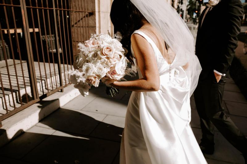 KWH real bride Shenea walking into her venue with her bouquet. She wears the Taryn Camille gown with scoop back and pockiets.