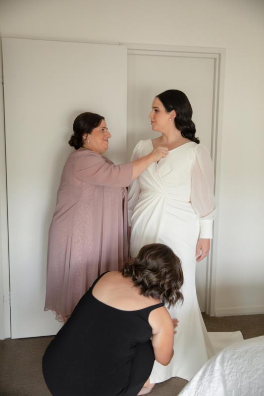 KWH real bride Dani has her mom help her get ready as she puts on her long sleeved Nikki wedding dress with short train.