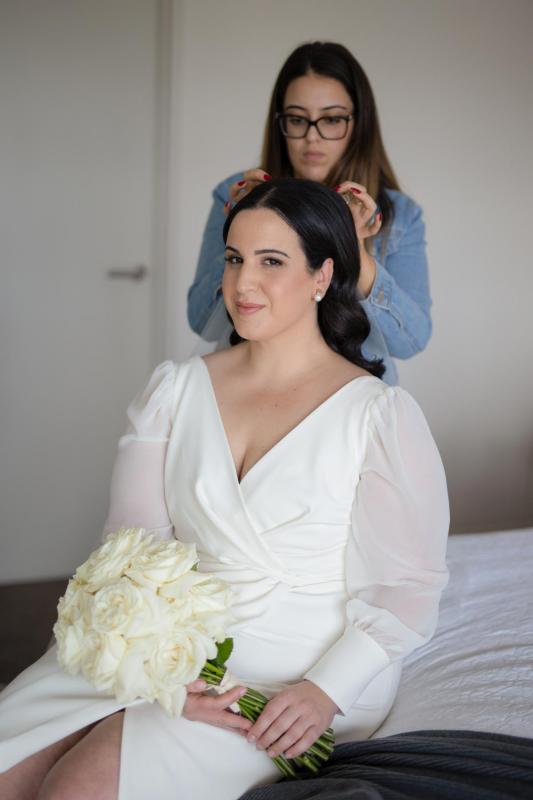 KWH real bride Dani has her veil put on as she sits wearing her ivory v-neck Nikki curve wedding dress.