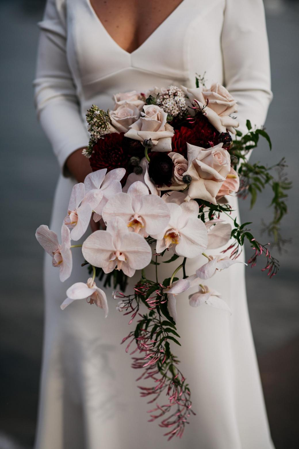 Bride Jordana holds her mixed bridal bouquet, featuring orchids and pink roses; whilst wearing the AUBREY wedding dress by Karen Willis Holmes.