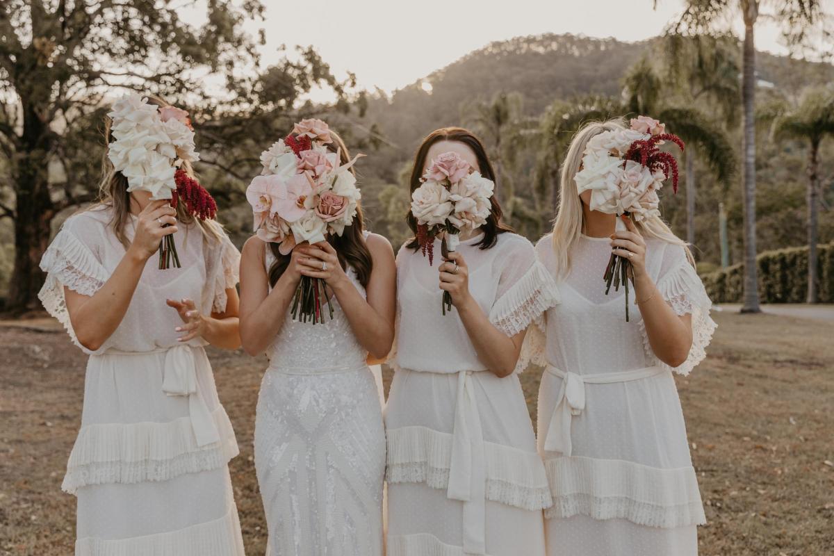 KWH bride Leah holding bridal bouquet with bridesmaids; featuring red, white, and pink roses.