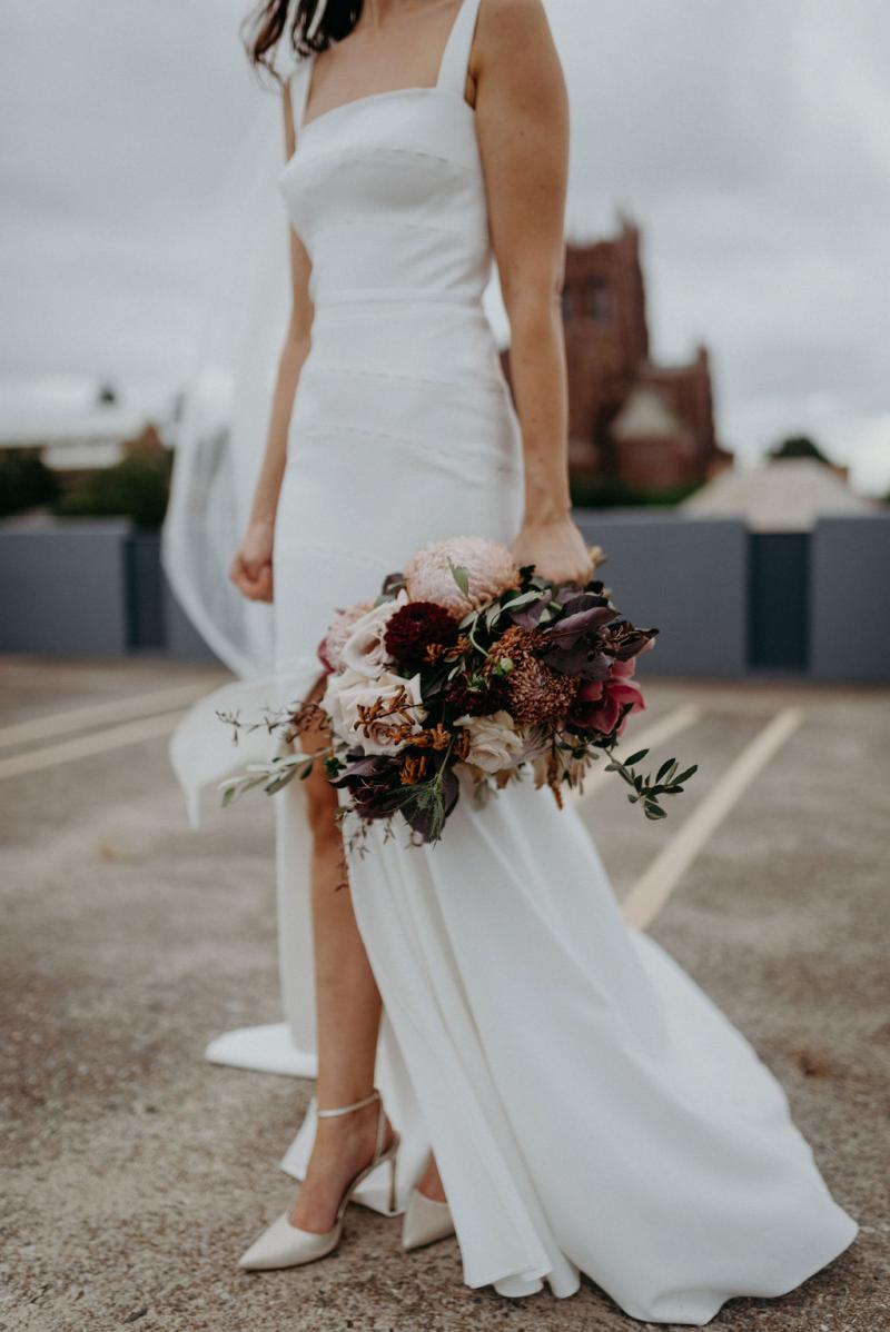 Bride wears elegant Violet wedding dress with split in skirt, heels showing and pink bouquet