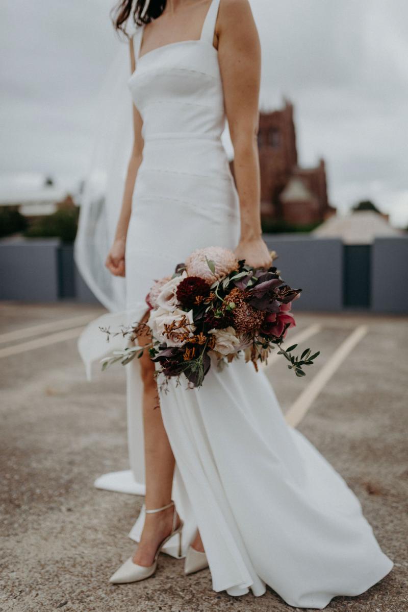 Bride wears elegant Violet wedding dress with split in skirt, heels showing and pink bouquet