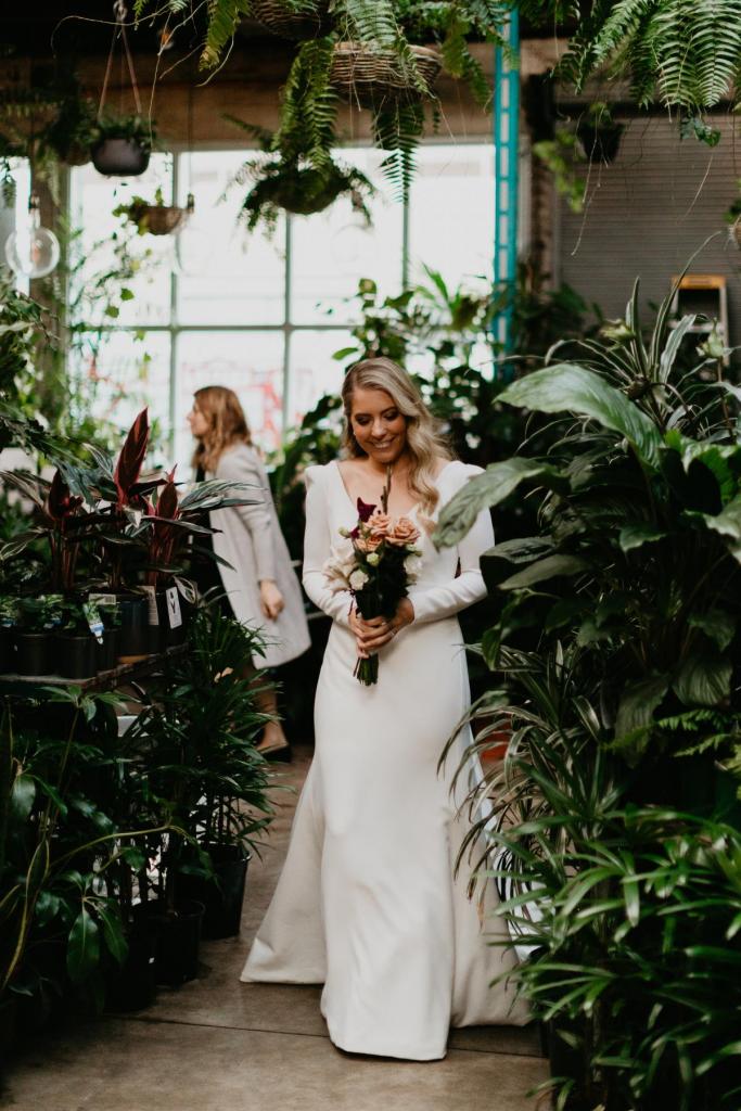 KWH bride Kara walking down the aisle, wearing the AUBREY gown; a long-sleeved elegant wedding dress.