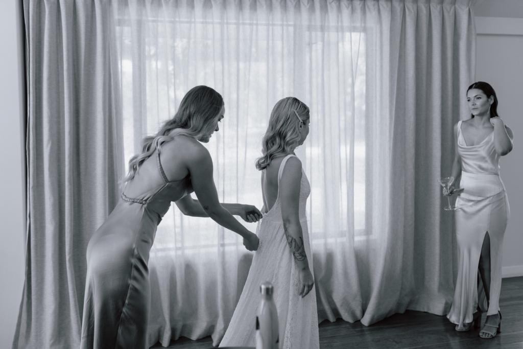 Karen Willis Holmes bride Megan getting ready with bridesmaids for romantic wedding, wearing the Nadia gown; an edgy and romantic lace wedding dress with a V-neck and side split.