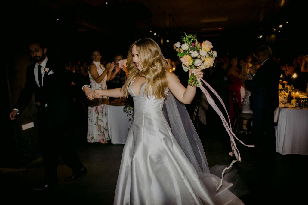 KWH bride Hannah at her festive wedding reception, holding her vibrant rose bridal bouquet and wearing the bespoke Taryn Nina gown, a timeless wedding dress.
