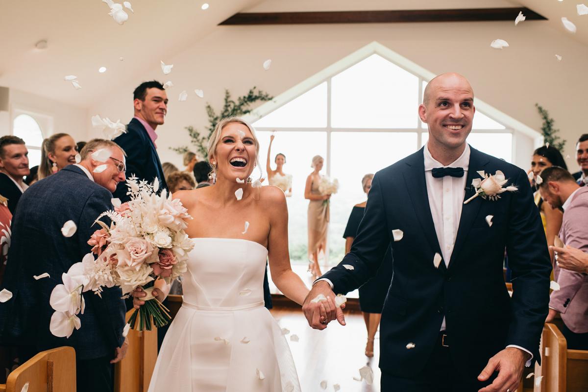 KWH bride Samantha and husband Adam walking down the aisle with petals being thrown over them. Bride wears the Esther wedding dress.