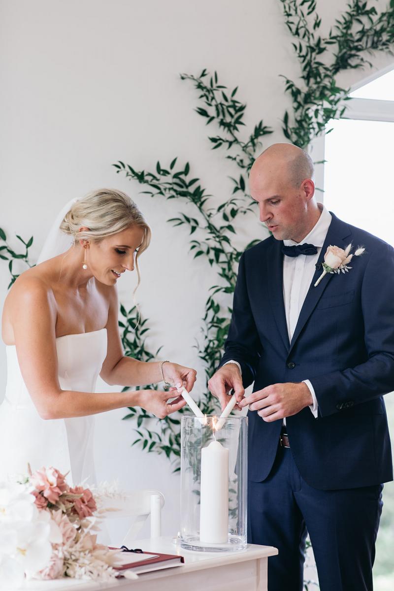 KWH bride Samantha and husband Adam lighting a candle together. Bride wears the Esther gown which features a front split, fitted base and long train.