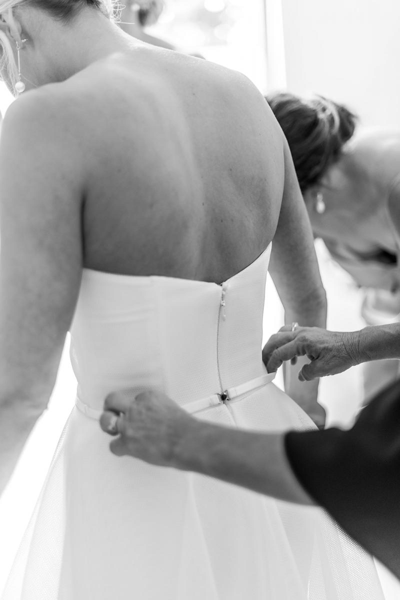 B&W image of KWH real bride Samantha getting ready and wearing the Esther strapless wedding dress with belt.