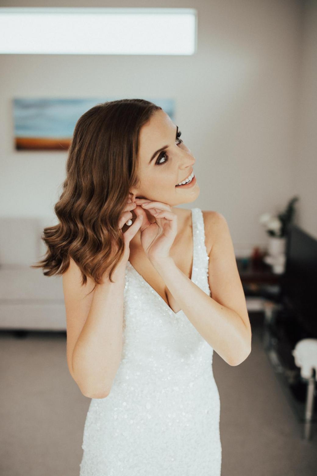 KWH bride Tash putting on her Amelie George earrings, wearing the Lola wedding dress.