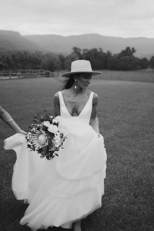 Real bride Sarah wears the Taryn Marina Bespoke wedding dress to her country wedding, posing with a straw fedora and native bouquet for wedding portraits.