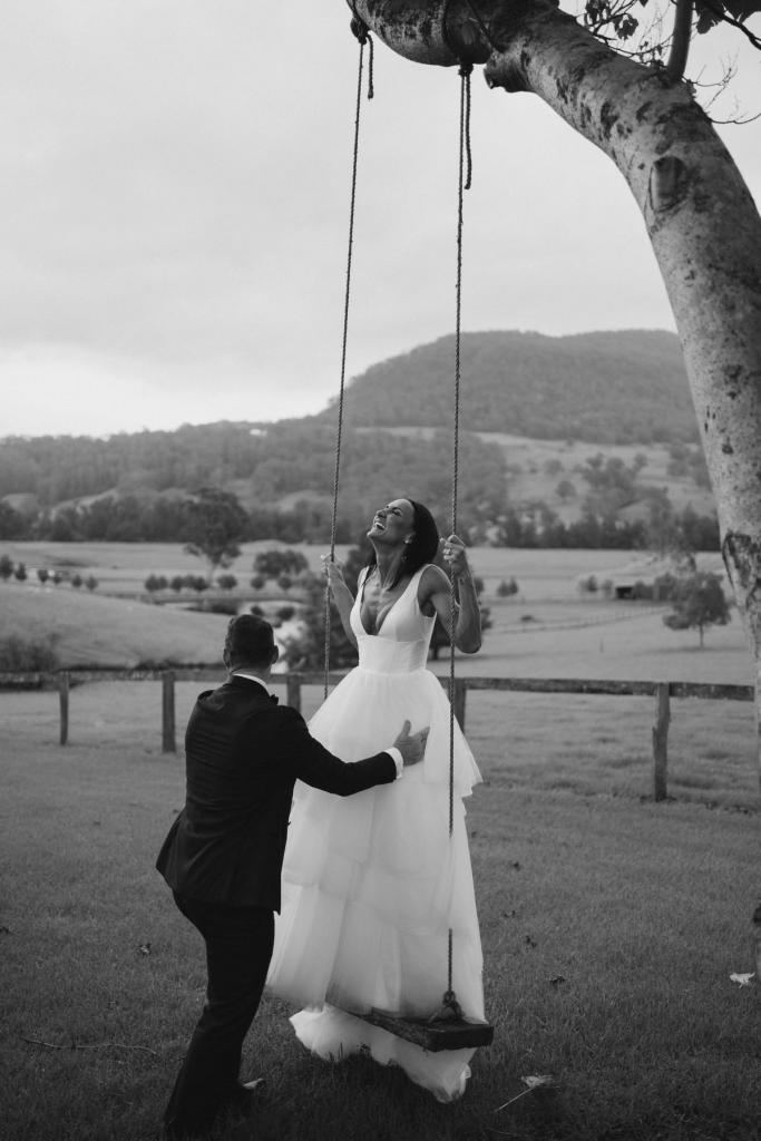 Real couple Sarah & Phil celebrate their country farm wedding, bride wears the Taryn Marina gown by Karen Willis holmes, bride sits on swing for wedding portraits.