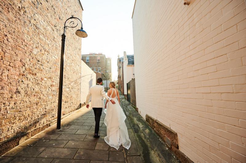 Real bride Claire wears the Cindy gown, a beaded halterneck wedding dress by Karen Willis Holmes while walking across the street with her husband.