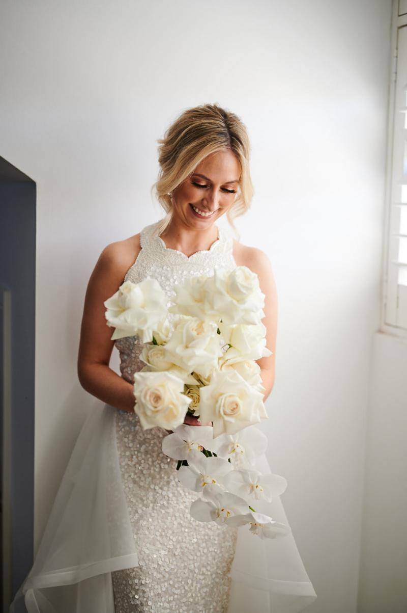 Real bride Claire getting ready for her Balmoral Beach wedding, wearing the Cindy gown, a beaded halterneck wedding dress by Karen Willis Holmes, holding an all white bouquet.