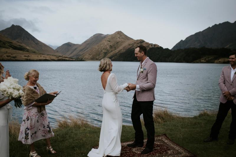 Lauren, KWH real bride, and new husband, Will, stand in front of epic Queenstown scenery as they say their vows. The bride wears the timeless Nikki wedding gown.