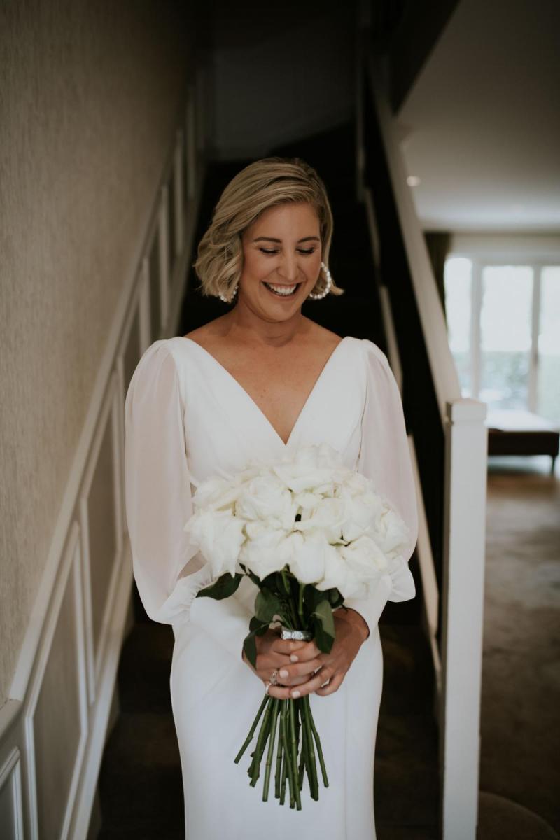 Real bride Lauren standing with her bridal bouquet while wearing the long sleeve Nikki gown from KWH.