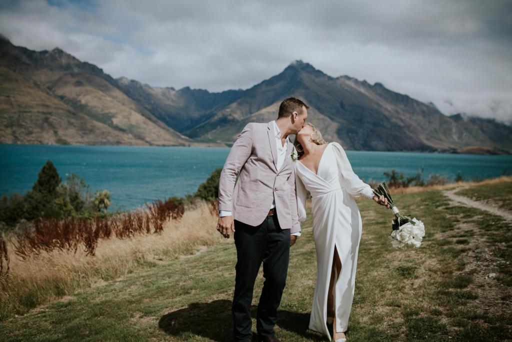 Real bride Lauren smooches her new husband in front of a dramatic Queenstown landscape, while wearing her Nikki gown from KWH.