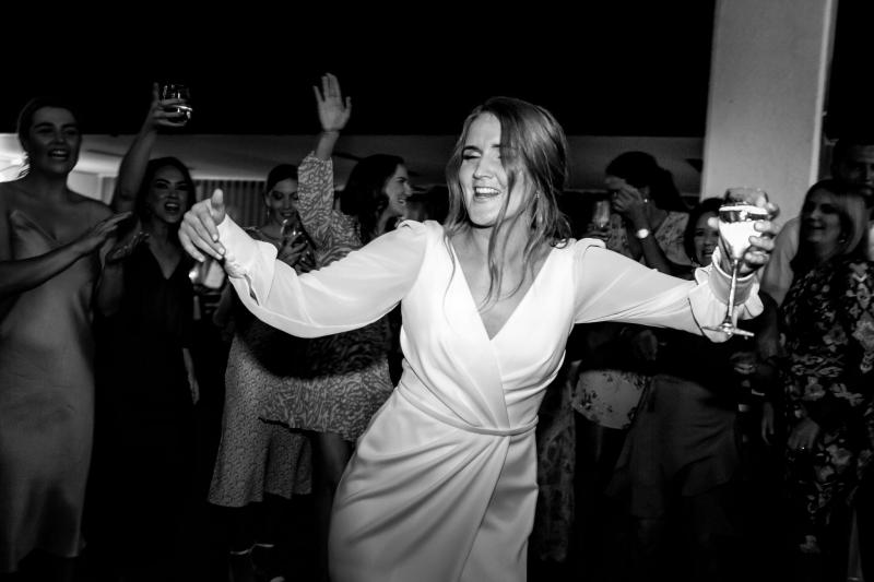 Real bride Shannon dancing at her wedding reception, wearing the long sleeve Nikki gown featuring a V-neck draped bodice.