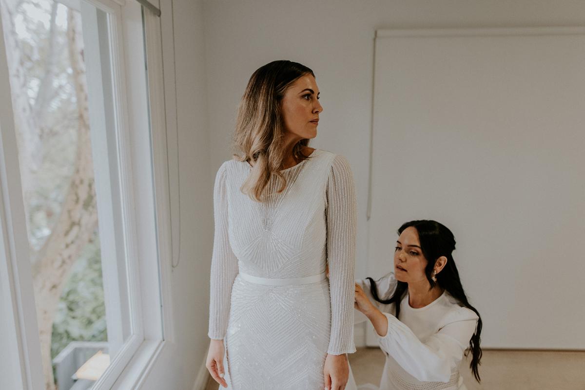 Real bride Penelope getting ready for wedding with bridesmaid, wearing the Cassie gown; a long sleeve art deco beaded wedding dress from the Luxe collection by Karen Willis Holmes.