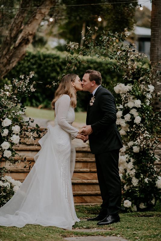 Real bride Penelope kissing at altar with husband David,wearing the Cassie gown and Oval Trains by modern bridal designer Karen Willis holmes.