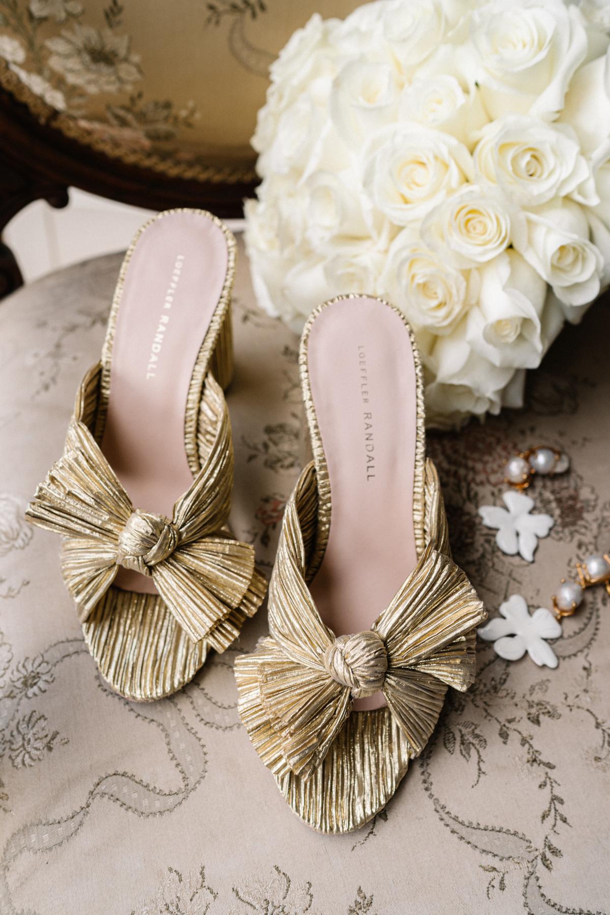 Real bride Maddi accessorises with unique old heels, statement white and gold earrings, and a white rose bouquet.